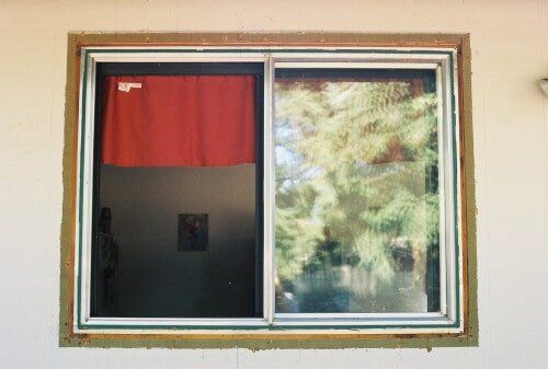A sliding window with one side closed with a red curtain, the other side showing a view of green trees.