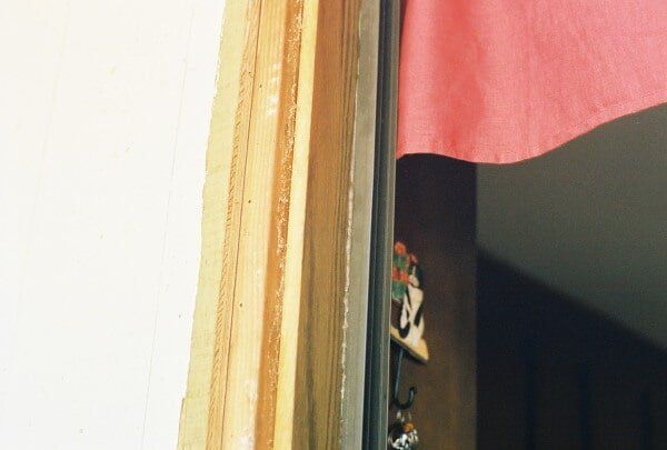 Wooden door frame with peeling paint next to a white wall and pink fabric.
