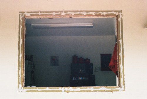 Open window frame in a white wall, revealing a room with a light fixture and objects.