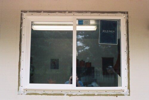 White-framed sliding window with reflective glass, installed in a stucco wall.