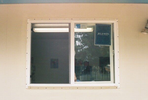 White-framed sliding window on a beige wall, with a partial view of an interior with a fluorescent light.
