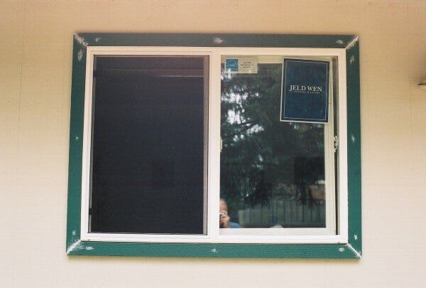 Green-trimmed window in a tan wall, one side covered in black material, the other clear.