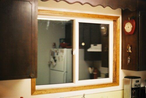 Kitchen window with wooden trim, reflecting a refrigerator and cabinets.