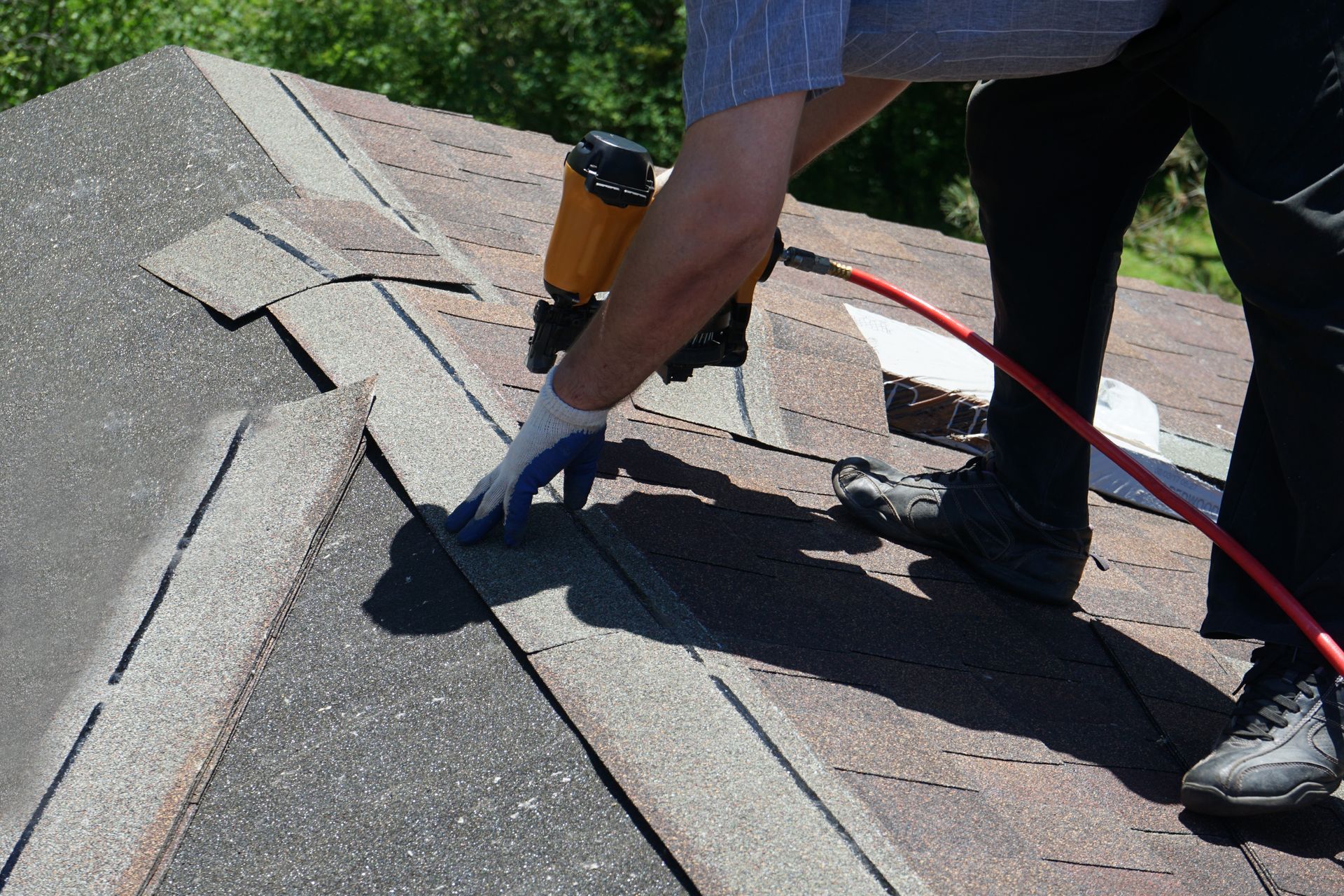 Worker using a nail gun to repair asphalt shingles on a roof