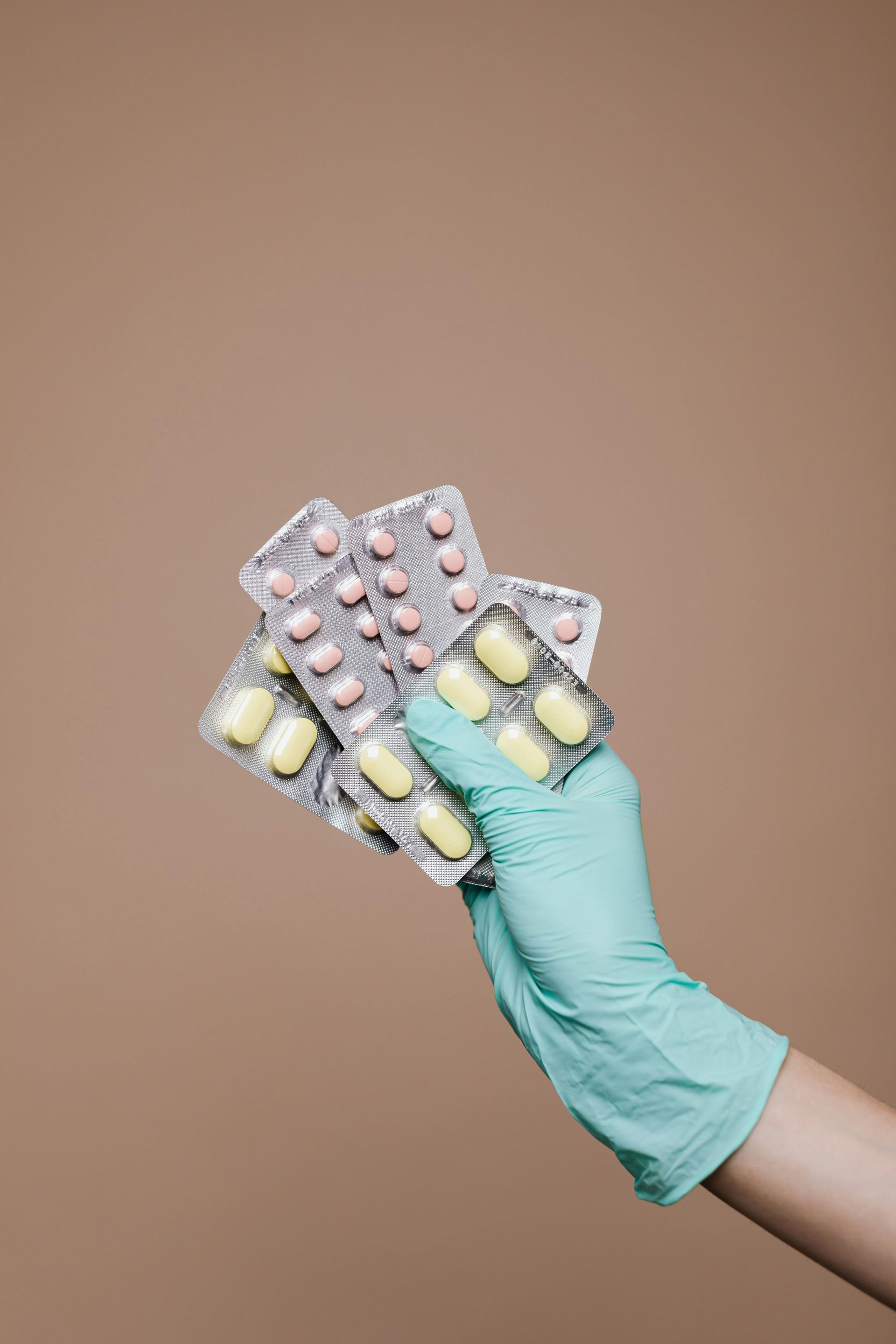 Hand in a teal glove holding multiple blister packs of pills.