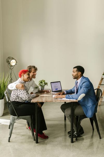 A couple embraces as they consult with a man at a table in an office setting.