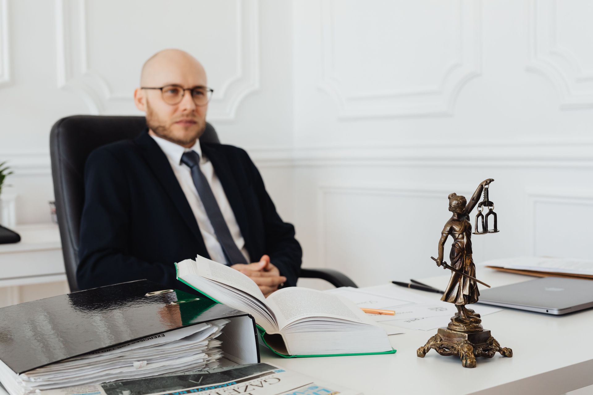 Lady Justice statue on a desk with an open law book and a defense attorney sitting in the background