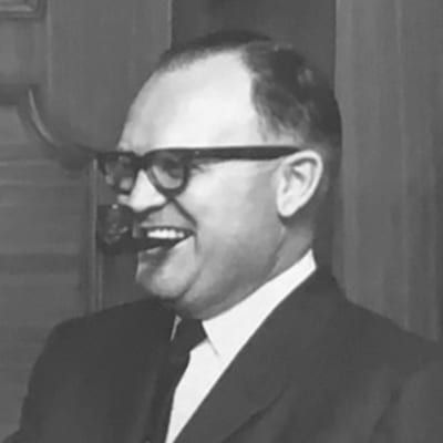 Agency founder H.E. Ferguson smiles in a suit and tie with a pipe in a black and white photo.