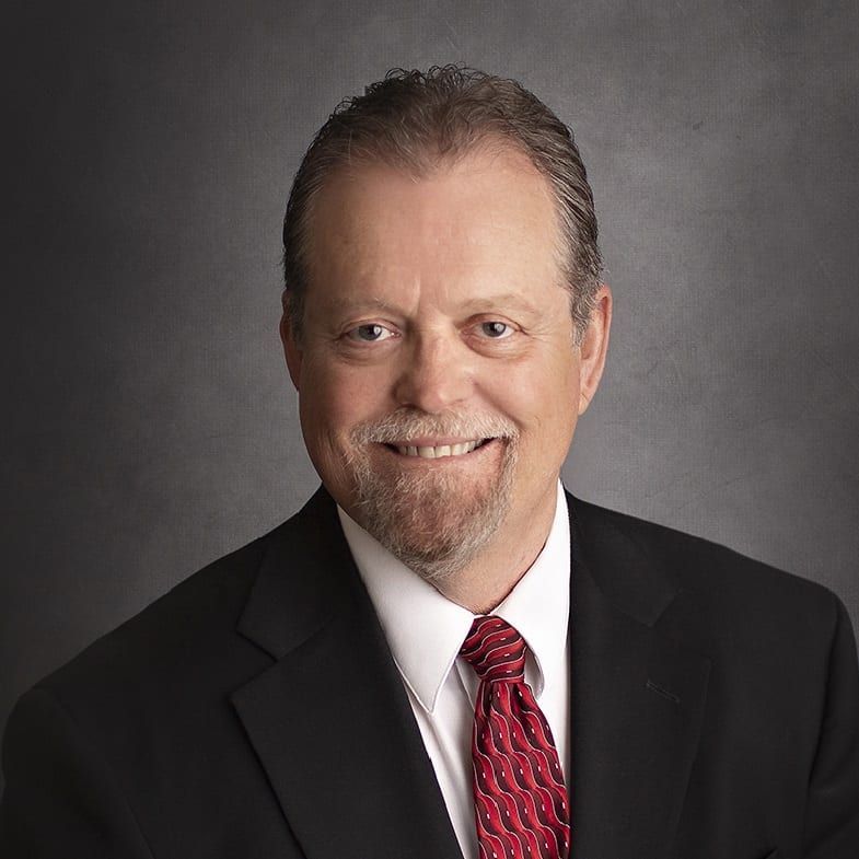Second-generation owner Perry Ferguson smiles in a black suit and tie.