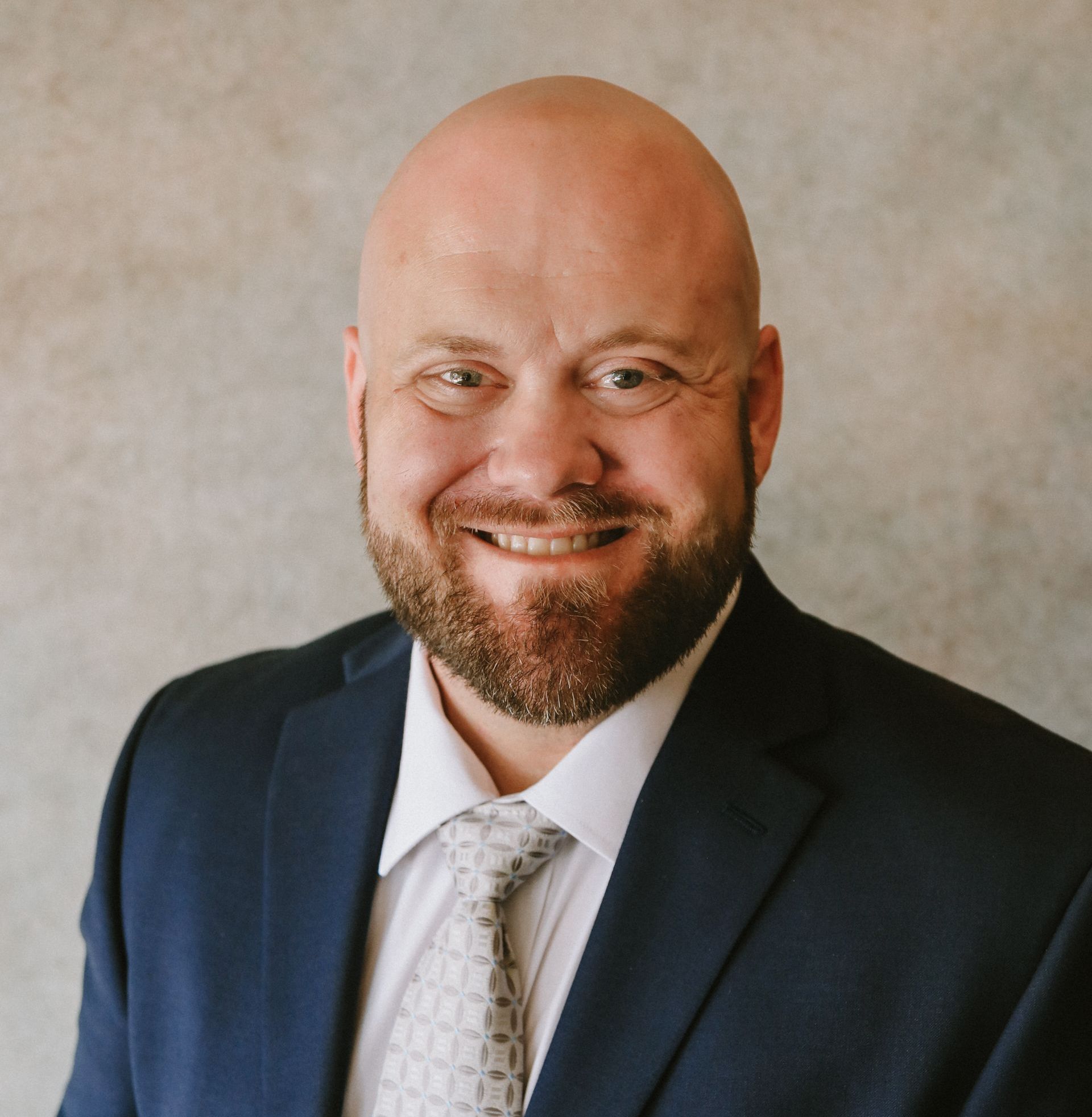 Third-generation agent Shane Ferguson smiles in a gray suit and tie in front of trees.