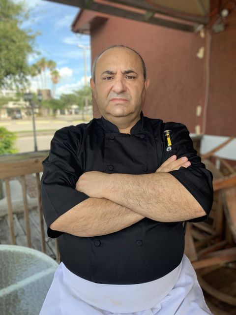 A man in a chef 's uniform is standing with his arms crossed.