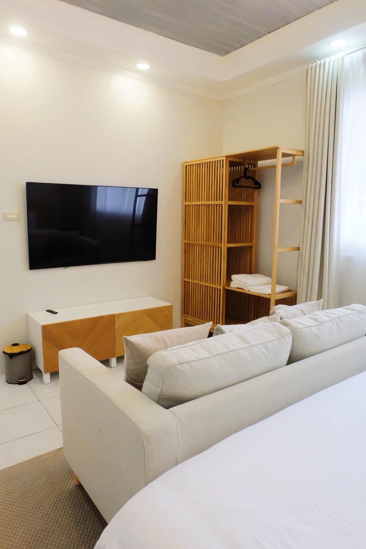 Bedroom with white sofa, TV, wooden shelving unit, and partially visible bed.