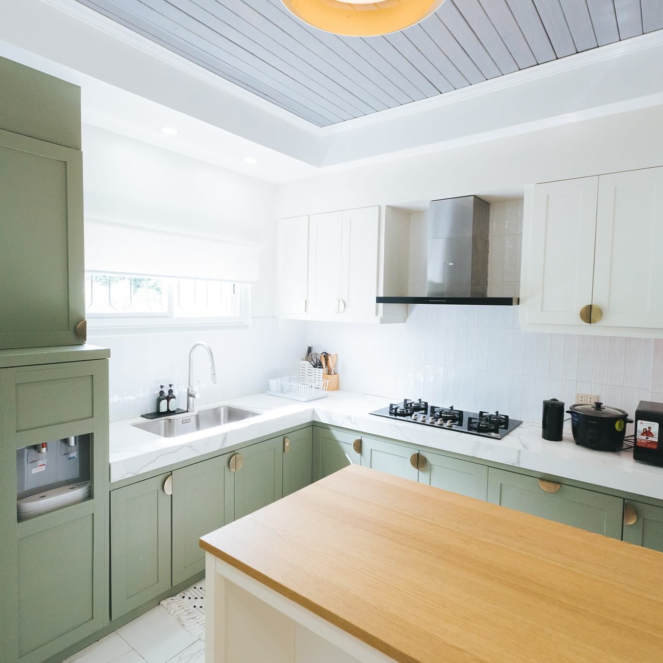 Green and white kitchen with wood island, sink, stove, and cabinets.