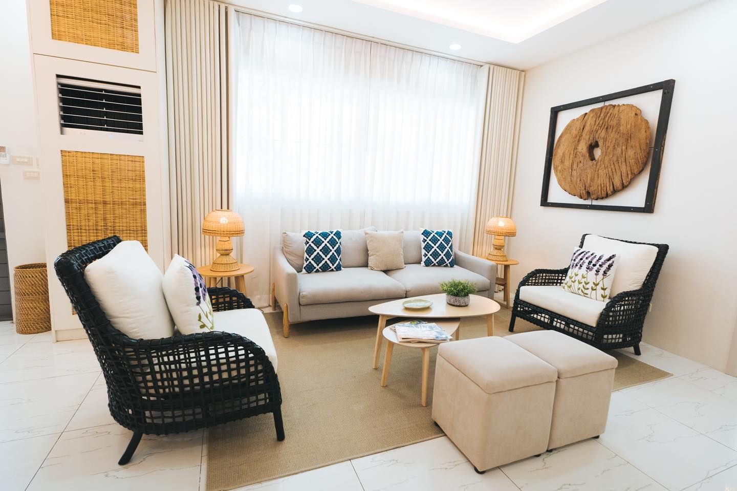 Living room with light-colored sofa, woven chairs, round coffee table, and decorative wall art.