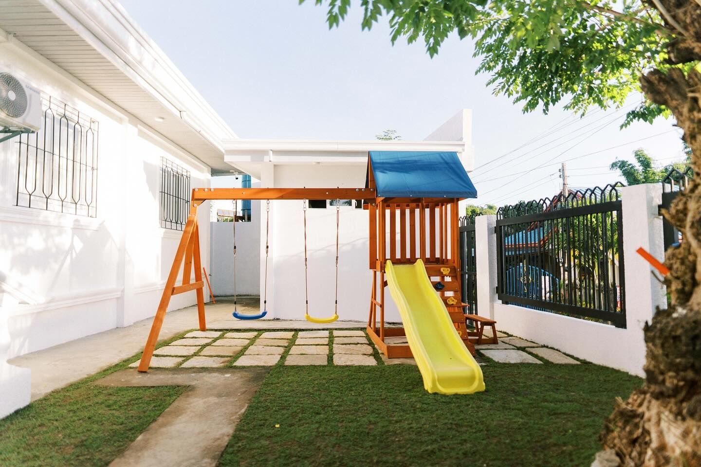 Playground with wooden swing set, yellow slide, and green lawn.