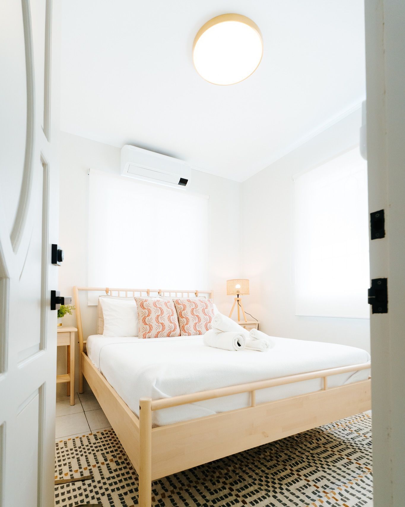 A bright bedroom interior with a bed, small rug, air conditioner, and closed door.