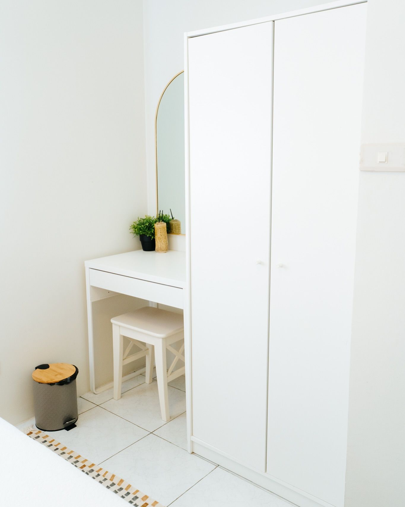 White vanity table with mirror and stool, next to a tall white wardrobe in a minimalist room.