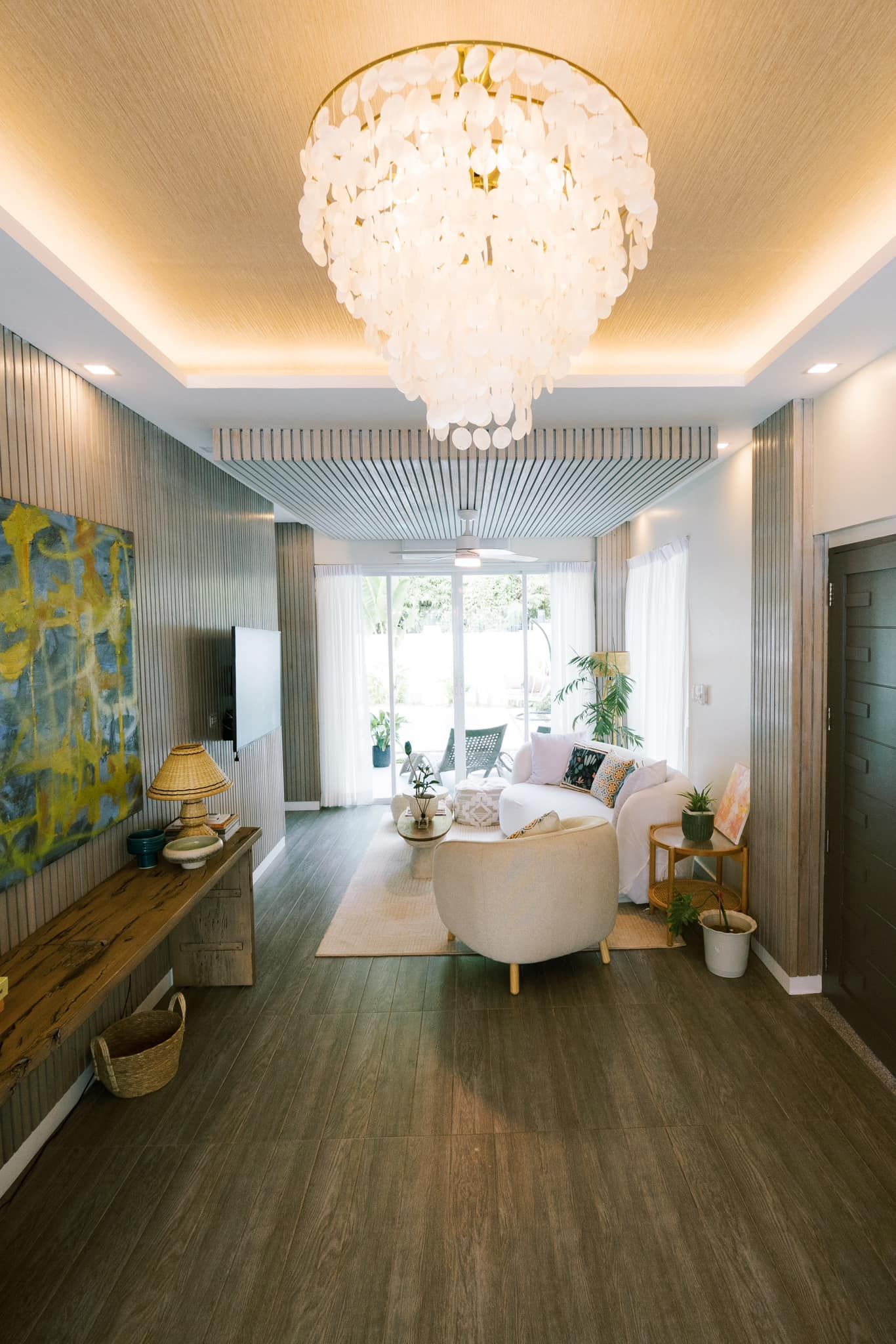 Living room with chandelier, sofa, and wood flooring. Features a balcony and artwork.