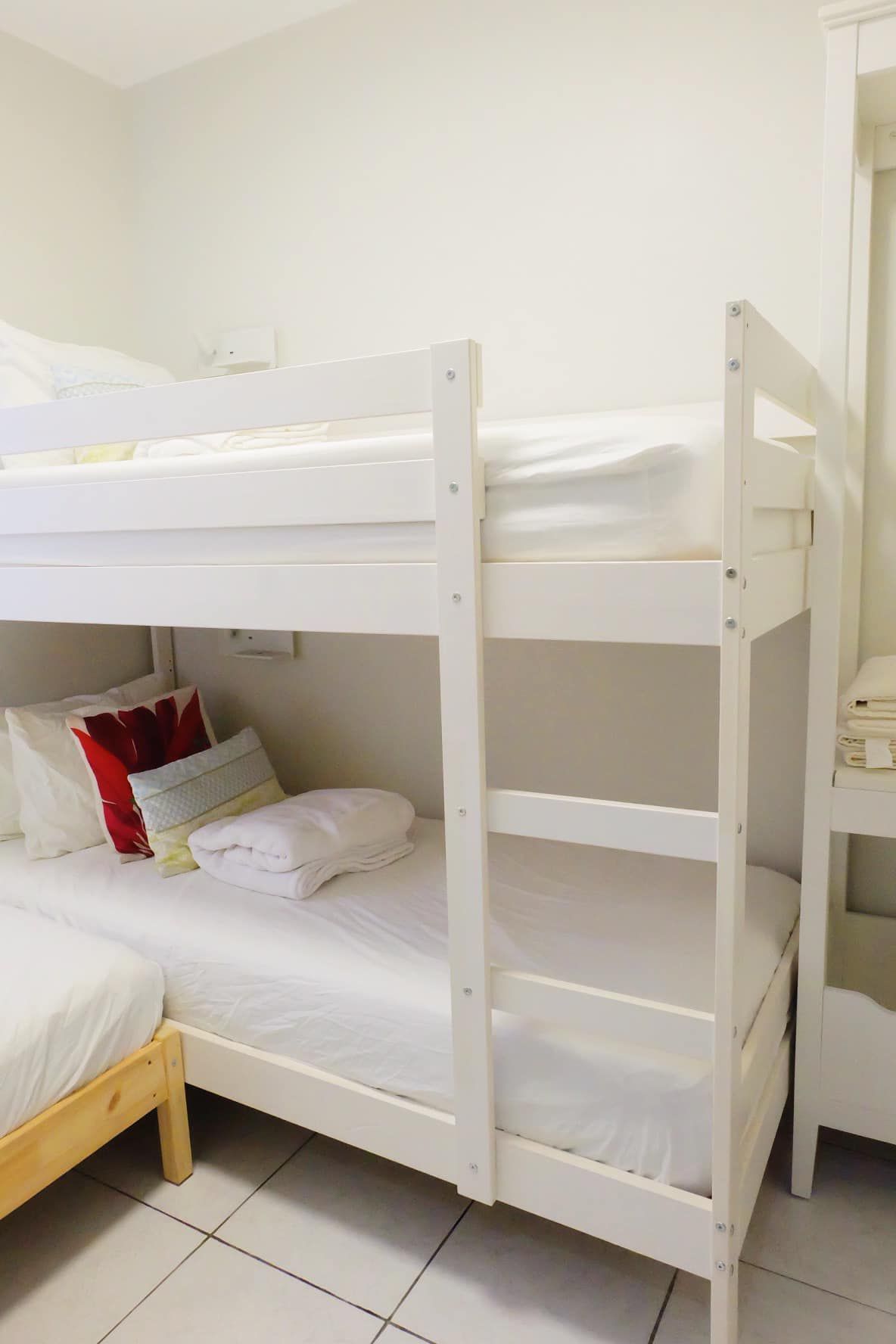 White bunk bed with bedding, pillows in a bright room.