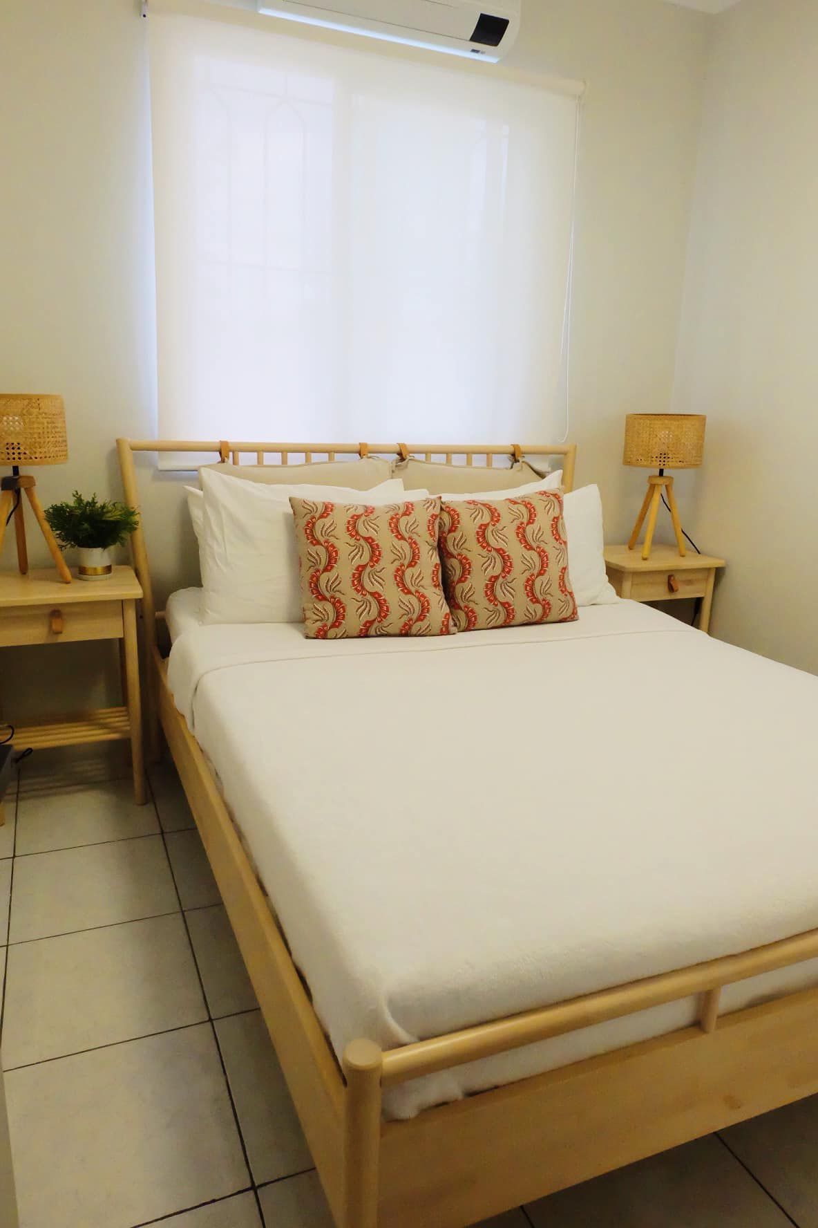 Bedroom with wooden bed frame, bedside tables, lamps, and white bedding. Window with sheer curtain.