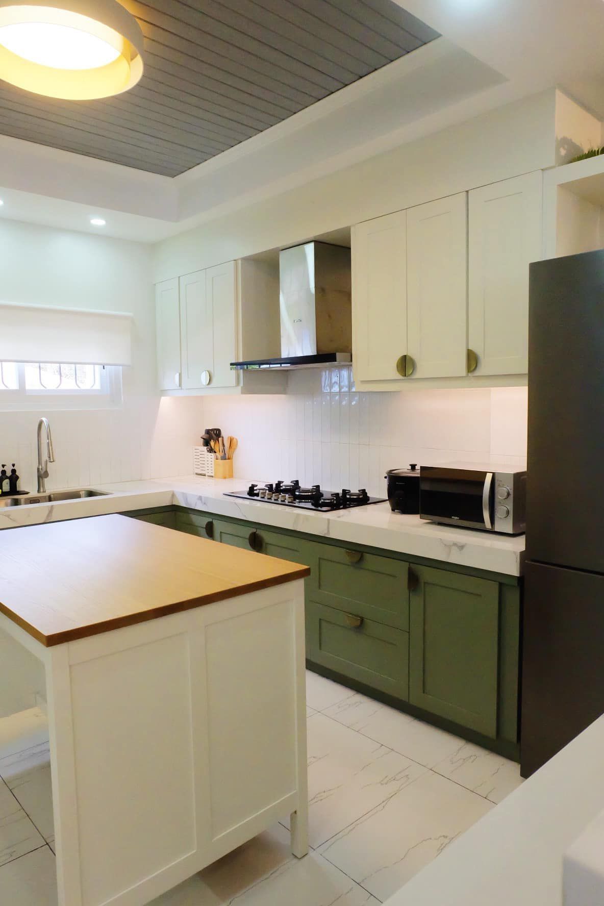 Kitchen with white and green cabinets, marble countertops, and a wooden island.