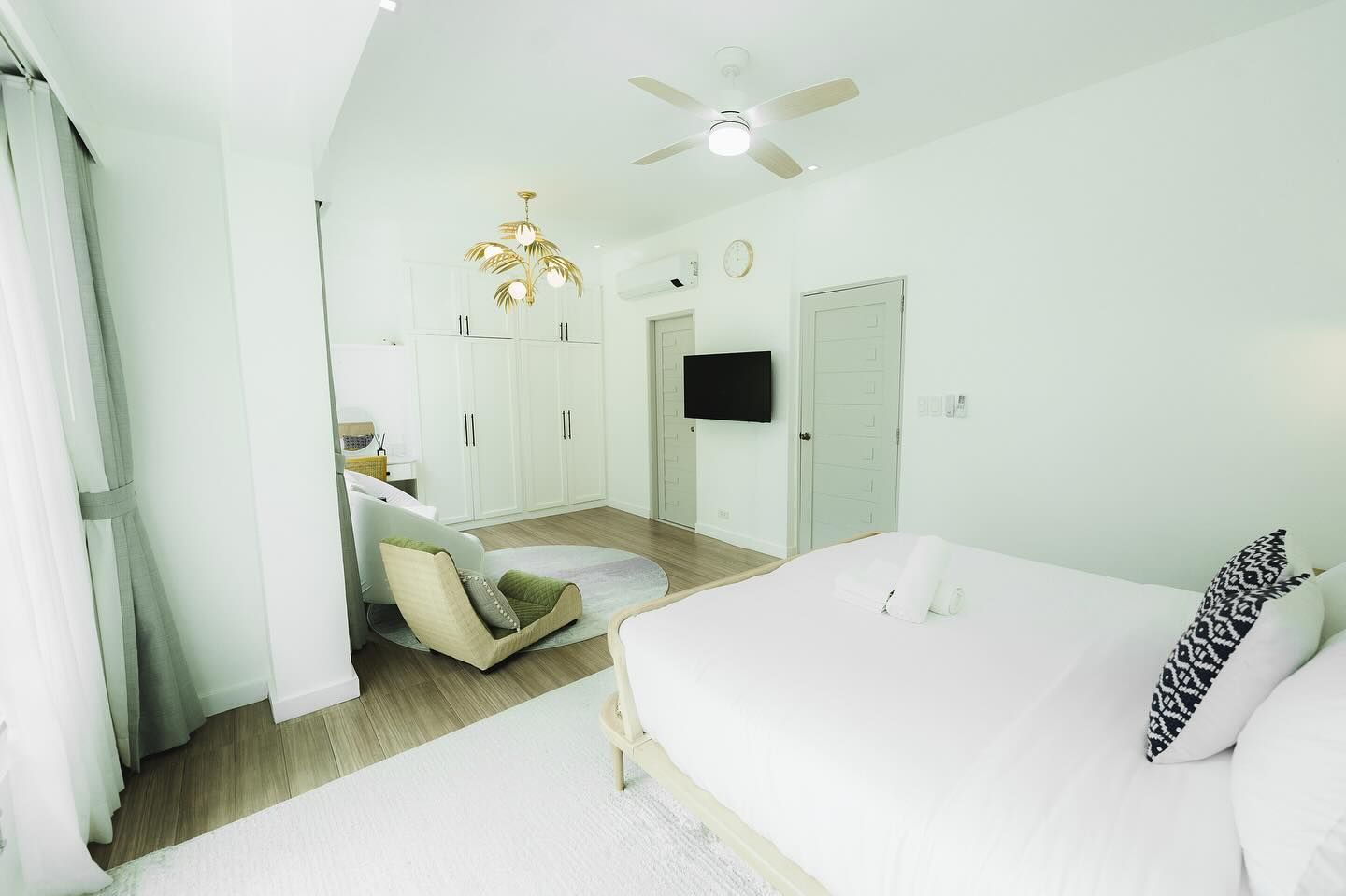 Bright white bedroom with bed, chair, and TV. Features light wood flooring and a round rug.