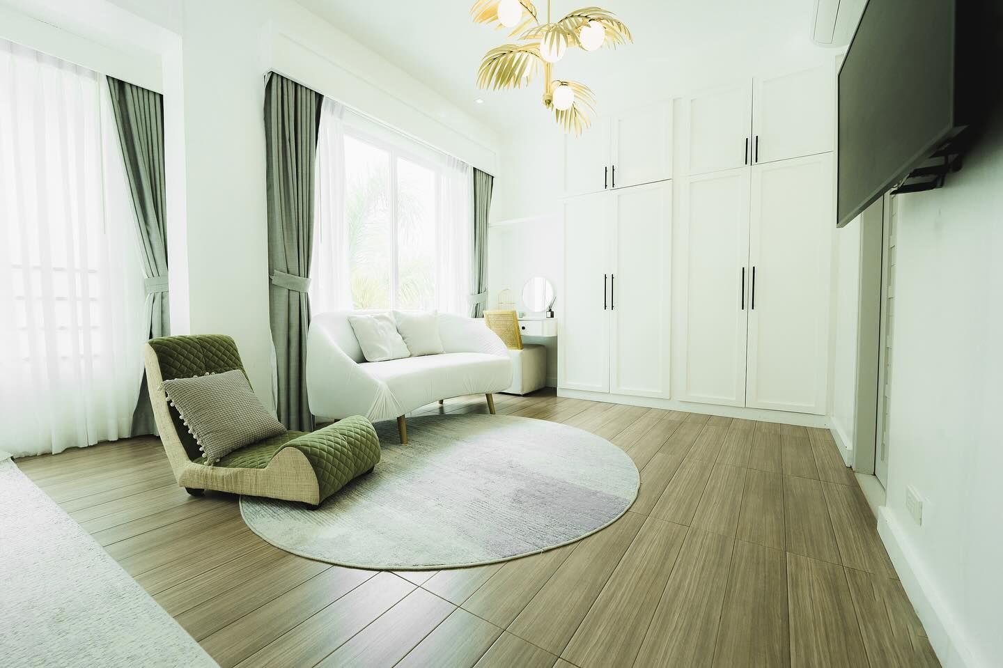 Bright bedroom with white walls, wooden floor, armchair, sofa, rug, wardrobe, and window with curtains.