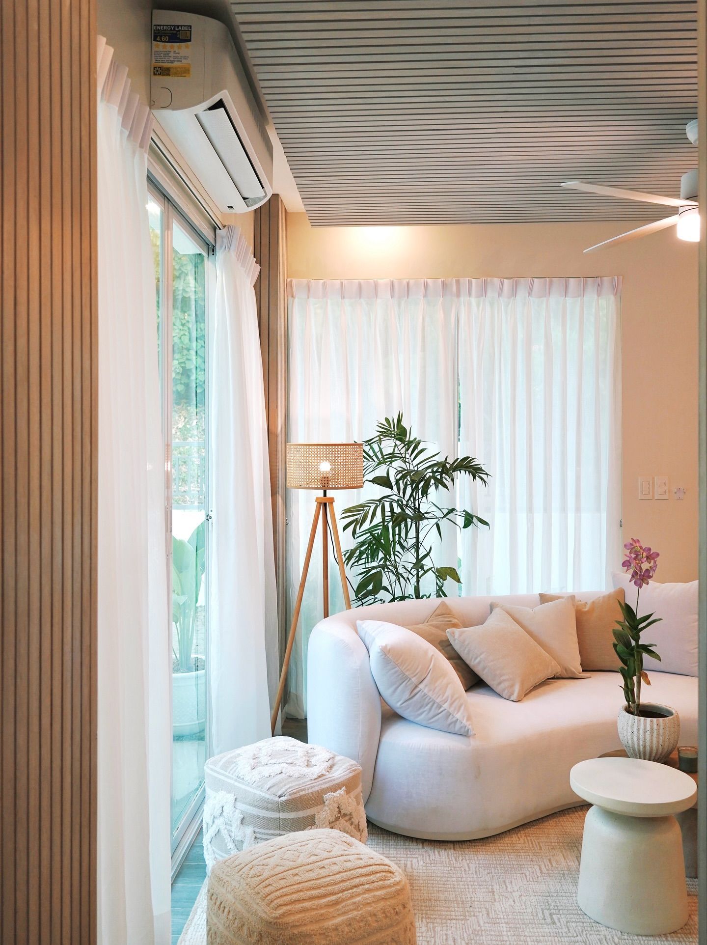 Living room with white sofa, sheer curtains, bamboo lamp, and a plant. Light and airy decor.