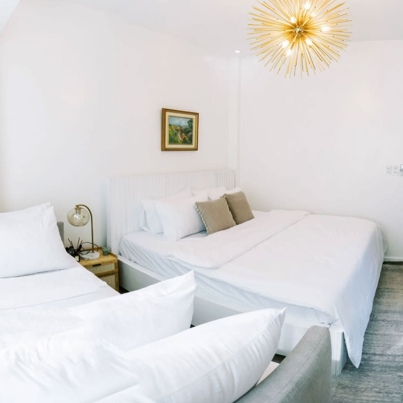 White bedroom with a queen bed, twin bed, and a sofa with white bedding, and a gold chandelier.