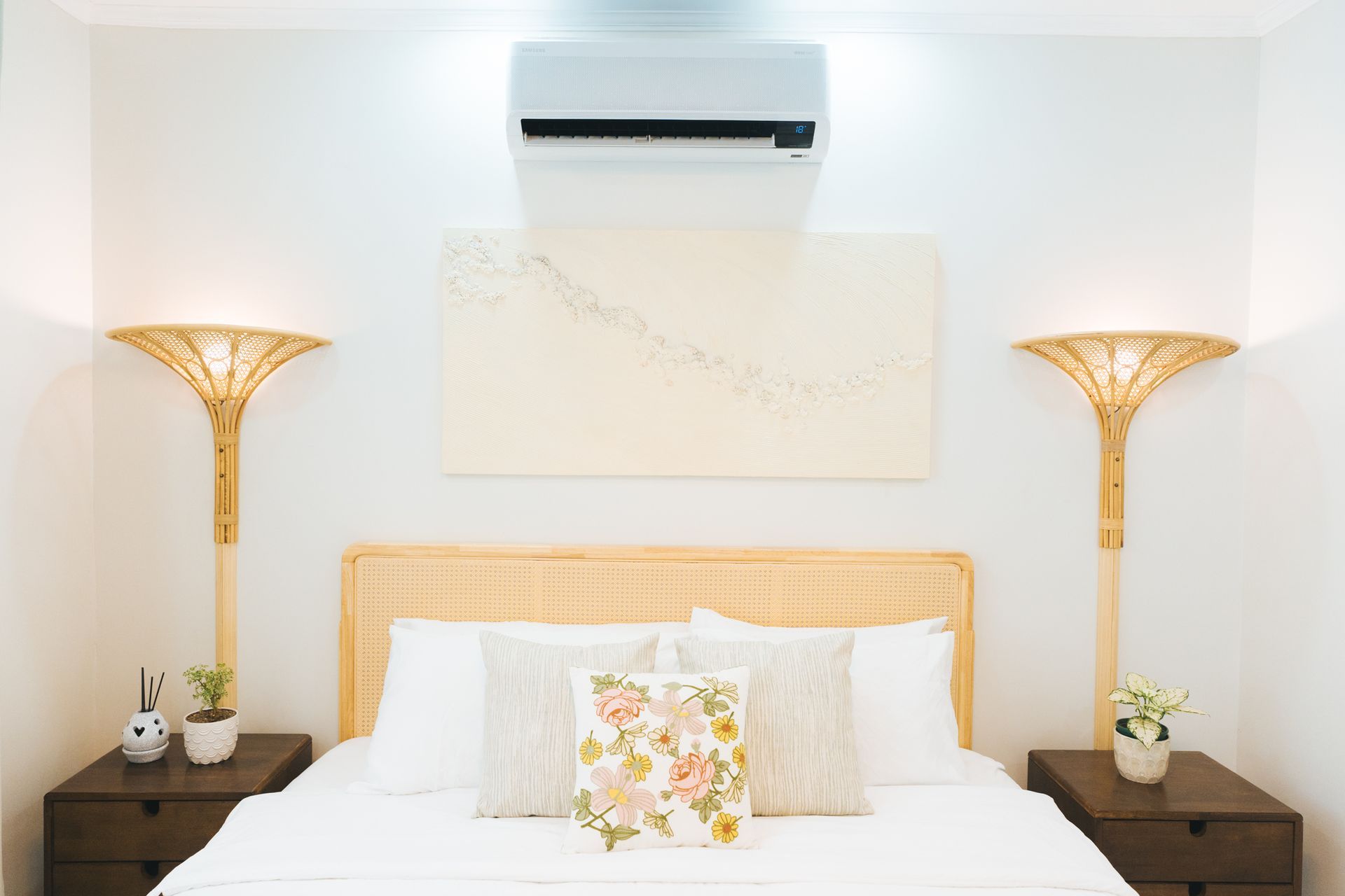 Bedroom with bed, art, bedside tables, lamps, and air conditioner. Neutral tones.