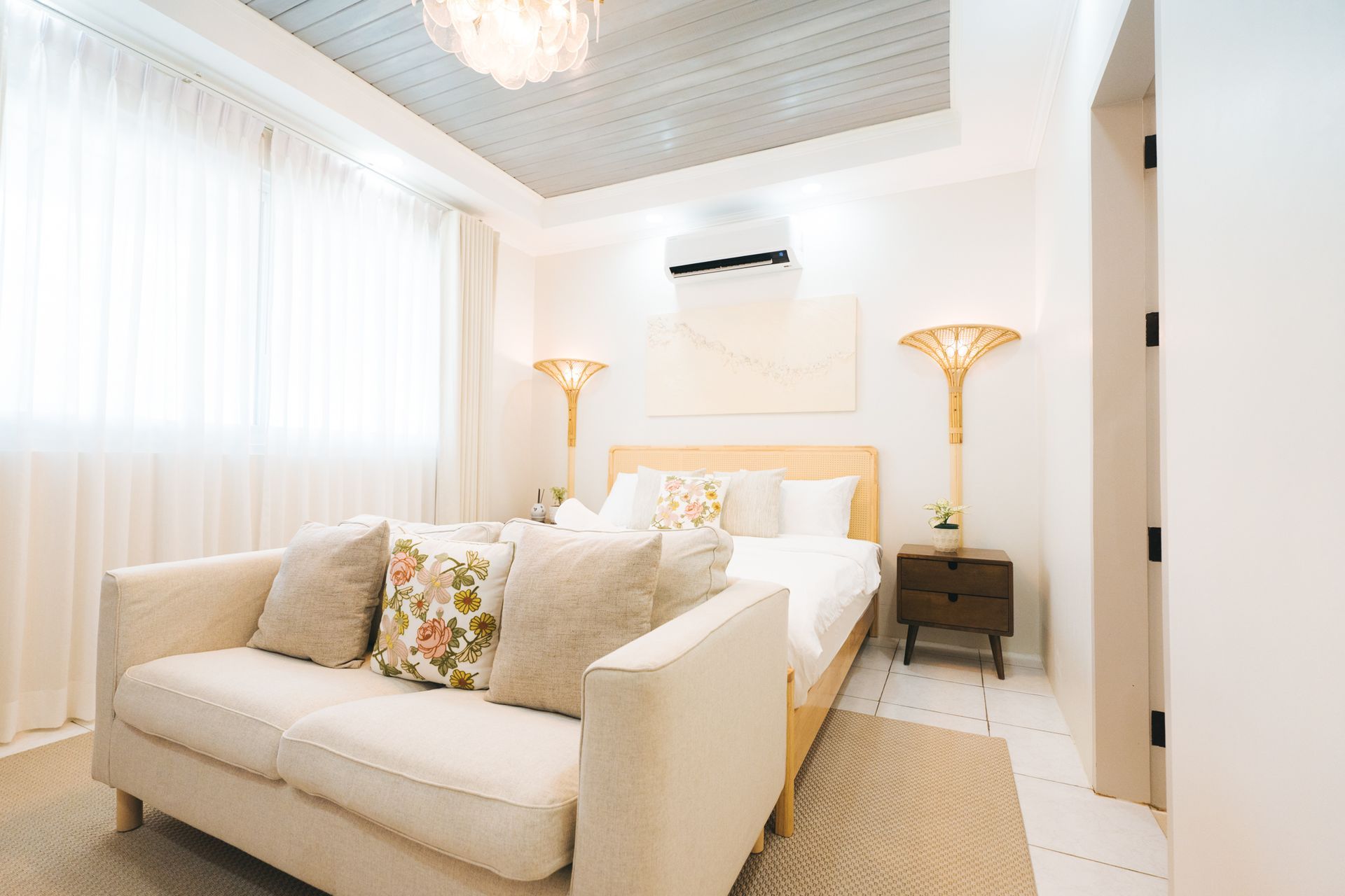 Bright bedroom with bed, sofa, lamps, and white curtains. Neutral colors, cozy atmosphere.