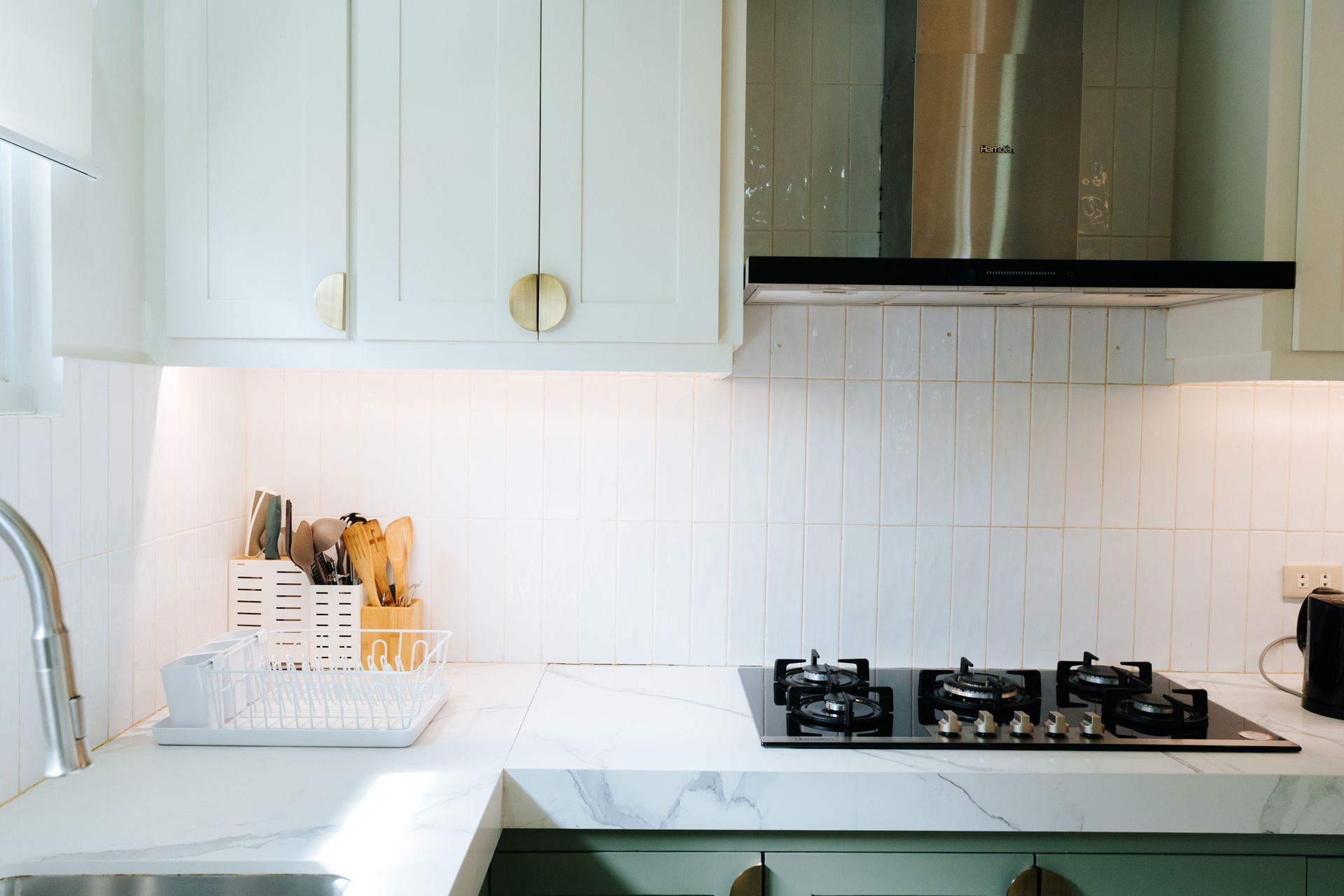 Kitchen with light green cabinets, marble countertop, and white backsplash, with a stovetop and range hood.