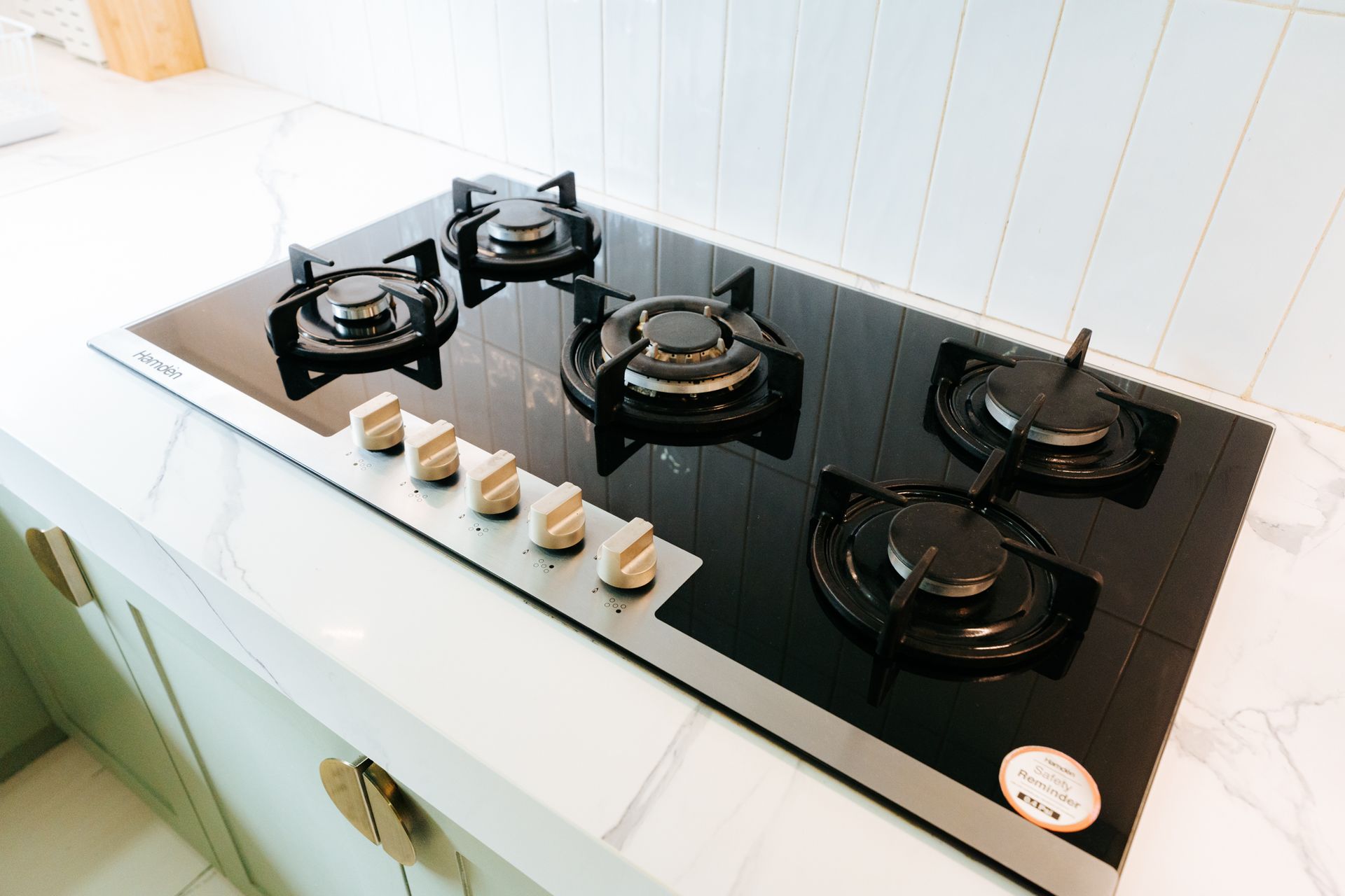 Black gas stovetop with five burners and silver knobs on a white countertop.