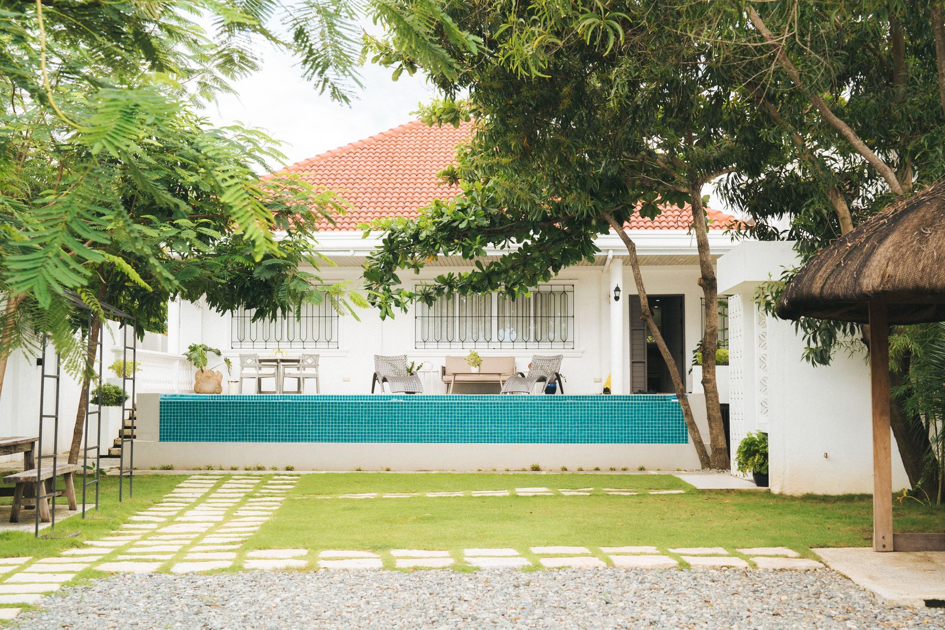 White house with red roof, turquoise pool, and surrounding green trees.