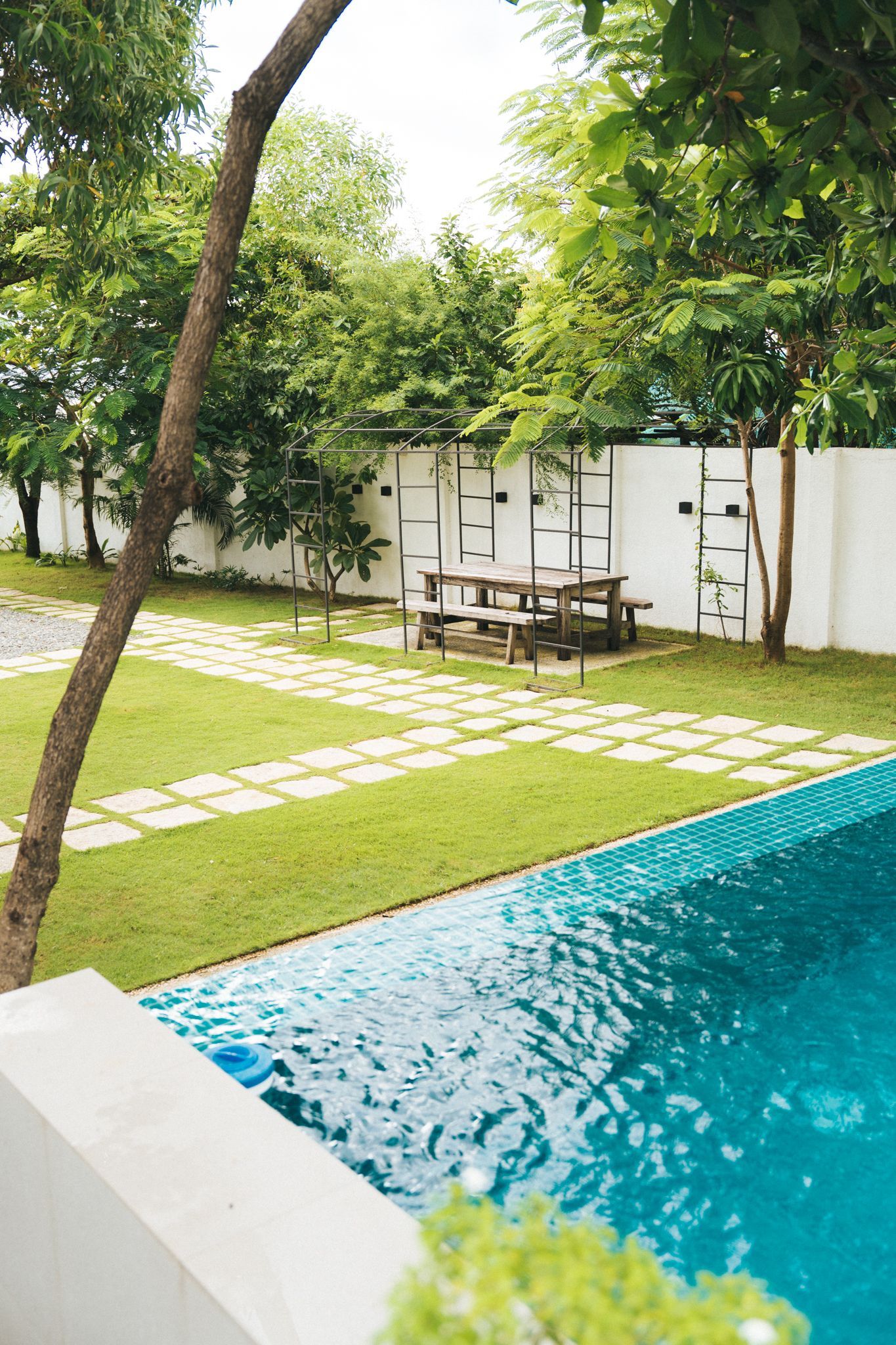 Swimming pool next to a grassy lawn with a picnic table and trees in the background.