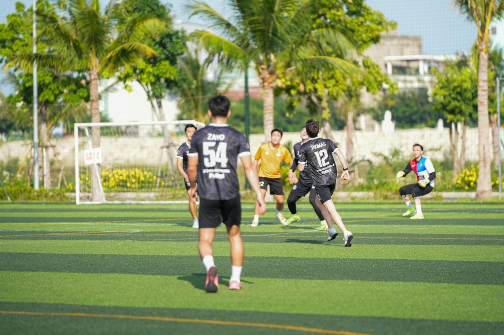 Men playing soccer on a green field under palm trees; players wearing jerseys, focused on the game.