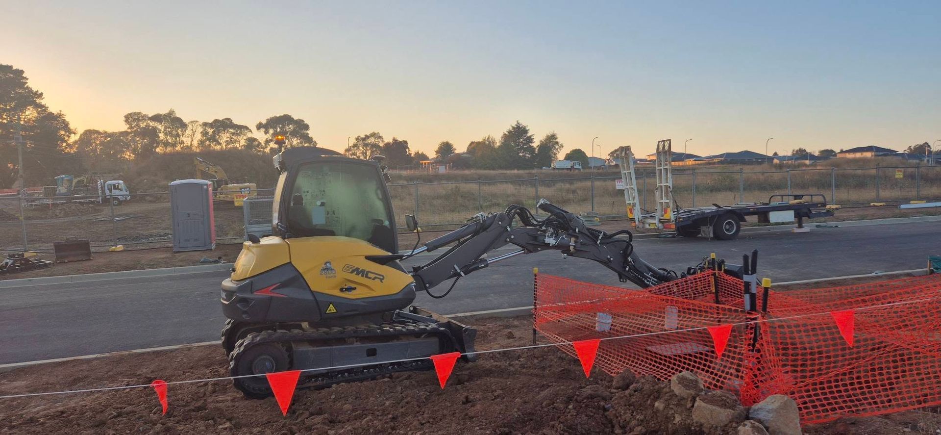 A yellow and black excavator is sitting on top of a dirt field.