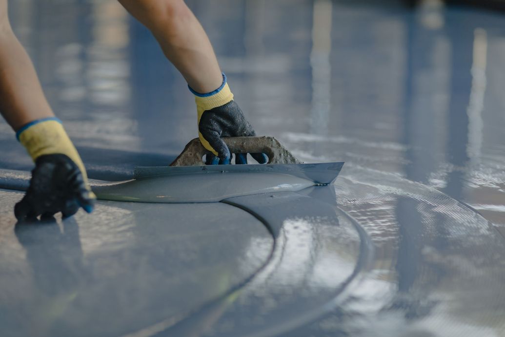 Person smoothing gray epoxy floor coating with a trowel, wearing gloves.