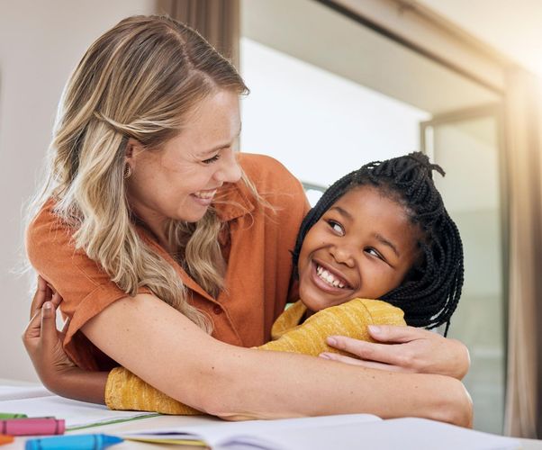 Woman hugs smiling child, bright setting.