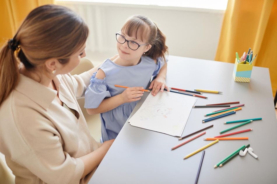 Therapist helping young girl with drawing during ABA therapy session