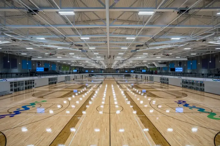 Large, empty indoor basketball facility with multiple parallel courts, polished wooden floors, and bright overhead lights.