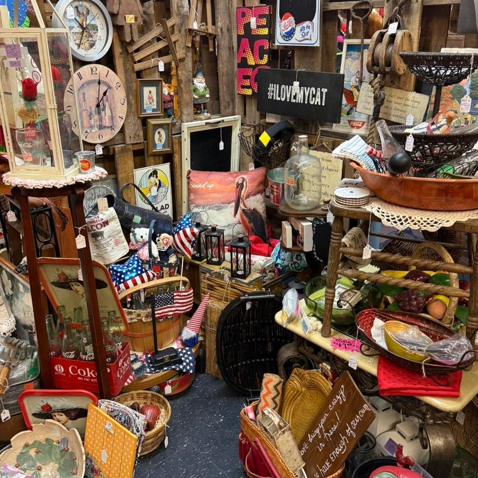A crowded antique shop interior featuring various vintage items, including wall clocks, a Coca-Cola crate, and decor signs.