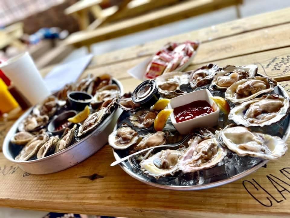 Two metal trays of fresh oysters on the half shell served with dipping sauce on a wooden table.