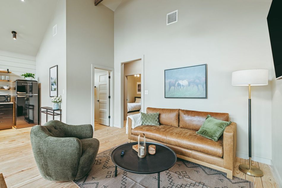 Modern living room featuring a tan leather sofa, a textured green armchair, a round coffee table, and wall art.