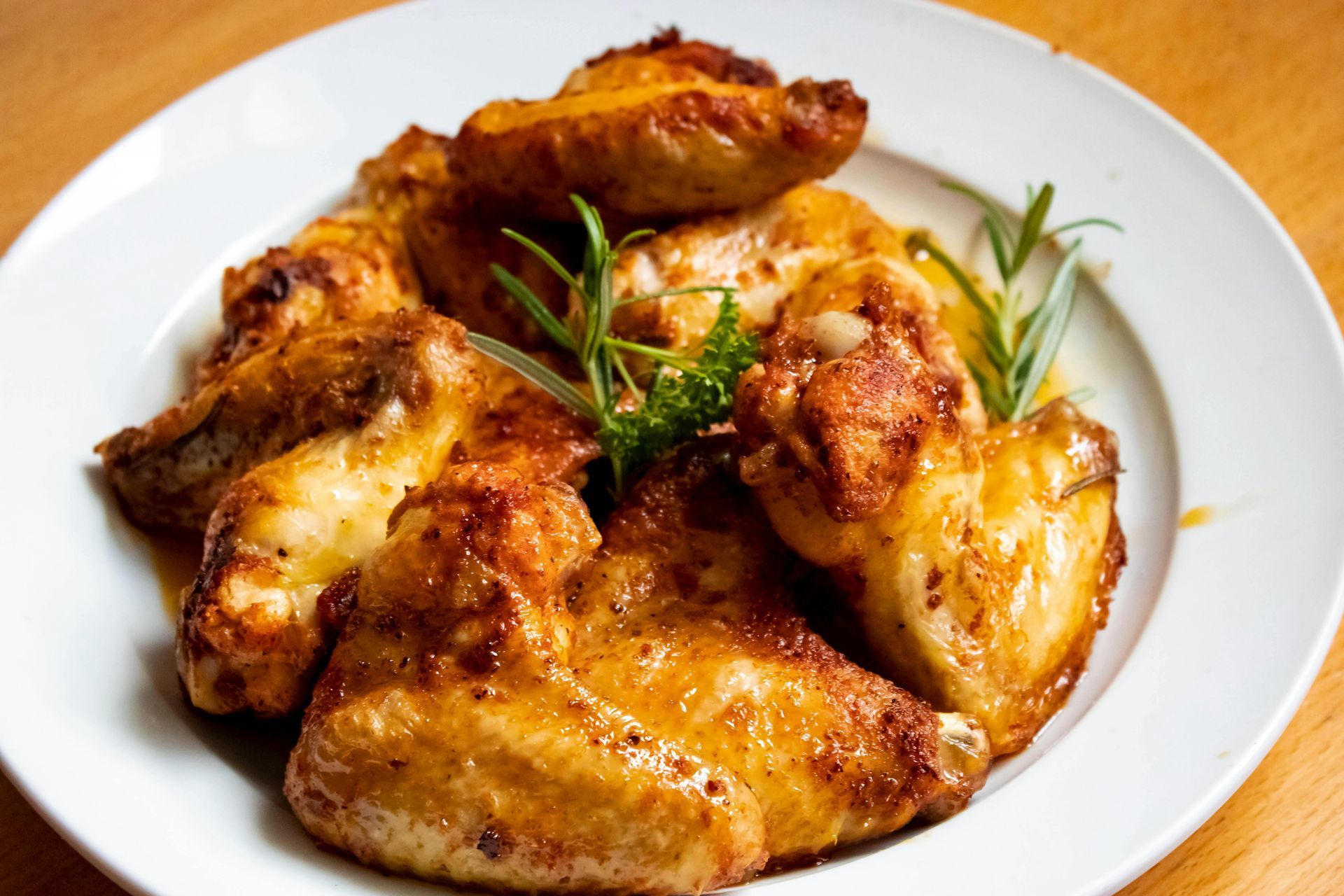 A plate of golden-brown roasted chicken wings garnished with fresh rosemary sprigs, set against a wooden table.