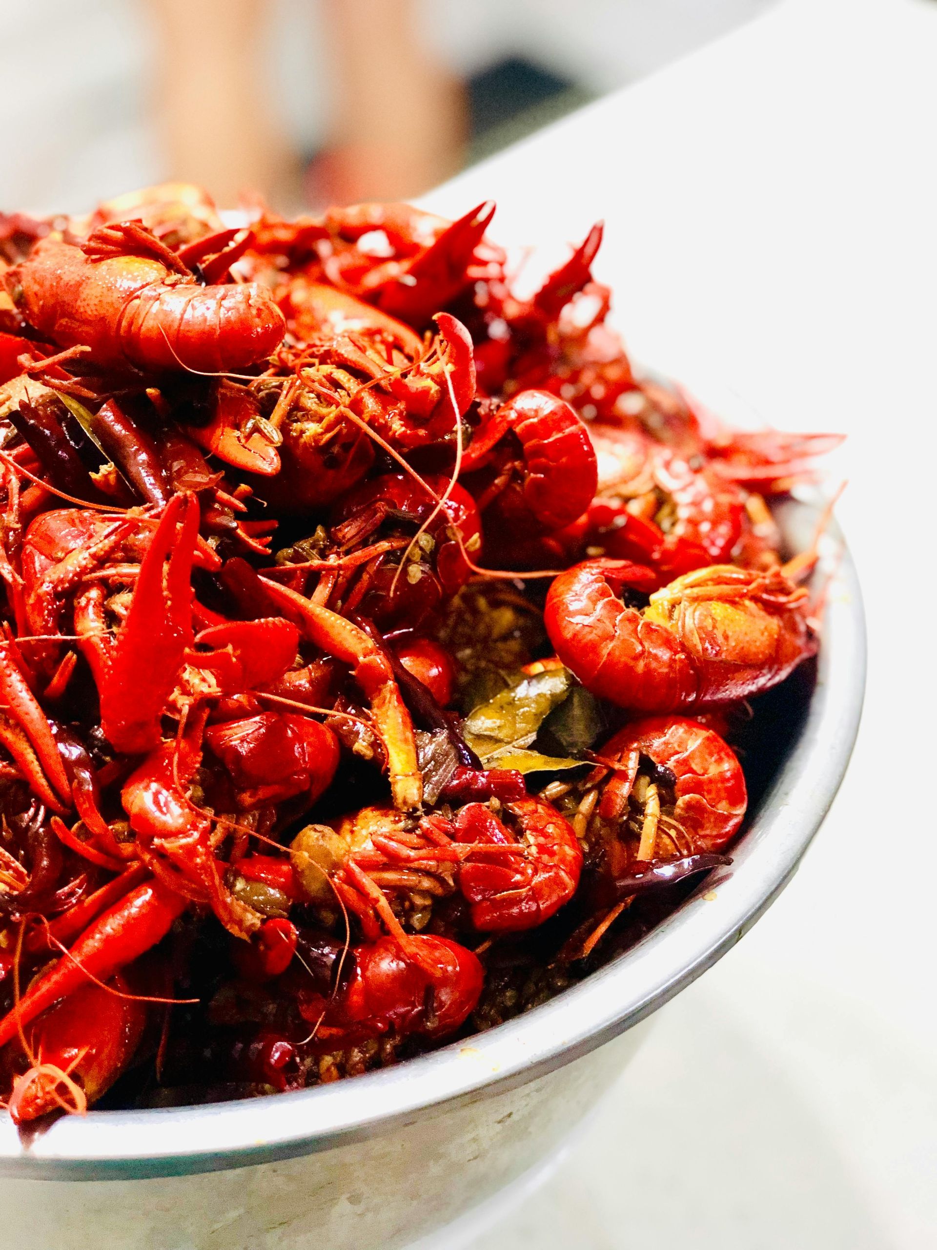 A large metal bowl filled with a pile of cooked, bright red crawfish seasoned with spices and herbs.