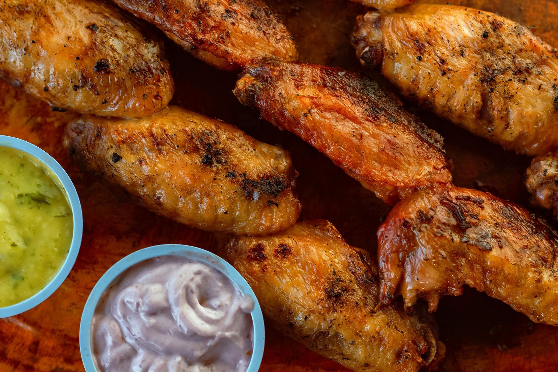 Roasted chicken wings arranged on a dark platter with small bowls of green and creamy purple dipping sauces.
