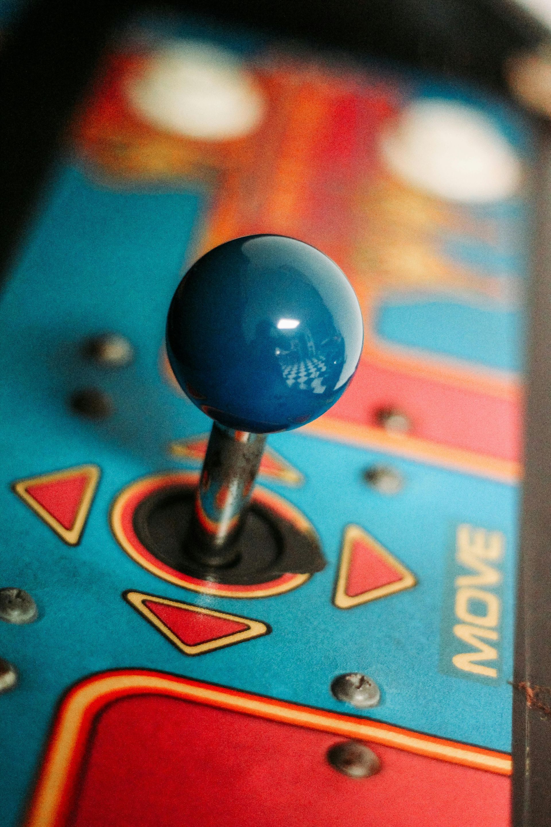 A close-up of a blue joystick on a retro arcade control panel with red and blue directional markings.