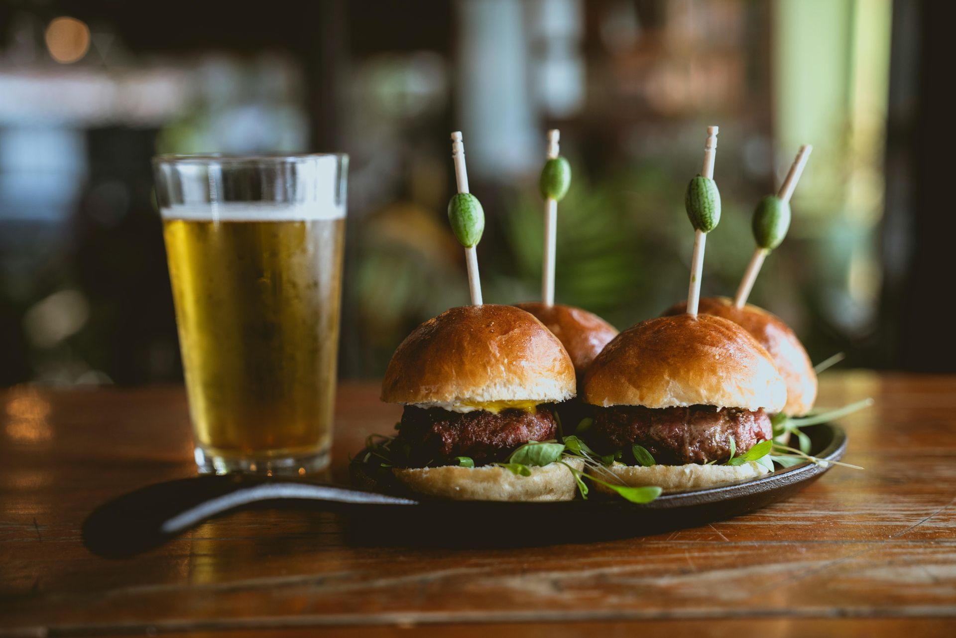 Four sliders on a small cast-iron skillet next to a glass of beer on a wooden table.