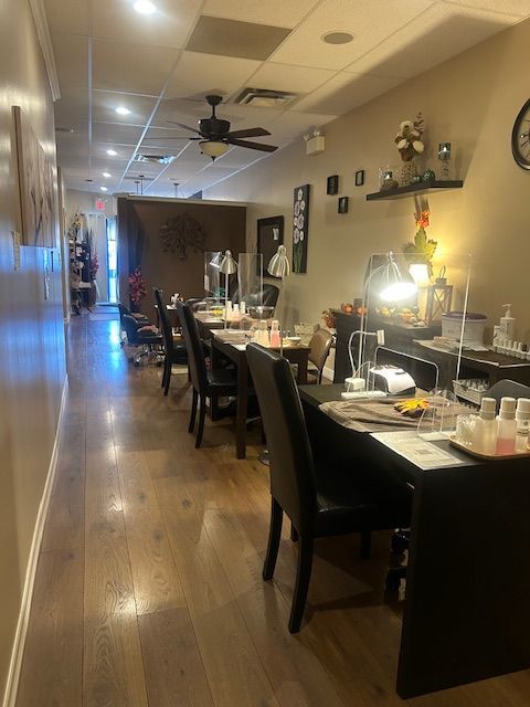 Nail salon interior with wooden floors, manicure stations, and chairs.